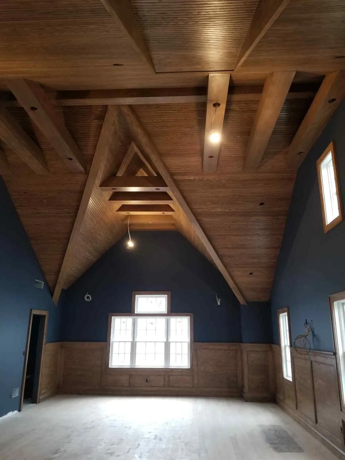 Finished room with a vaulted wood ceiling, exposed beams, navy walls, and wood wainscoting